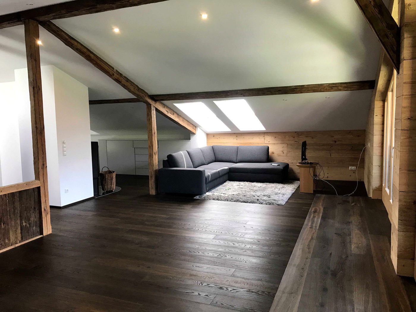 Wohnraum mit Ecksofa, dunklem Holzboden und Dachfenstern