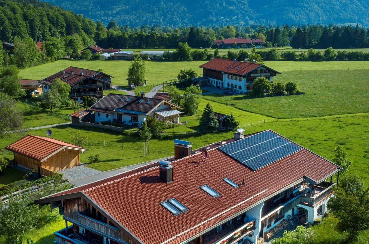 Luftbild über Schärfen: der Gasperhof im Vordergrund, dahinter Wiesen, Höfe und die Berge des Tegernseer Tals